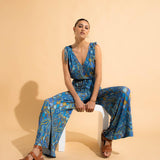 Woman wearing a blue patterned jumpsuit sitting on a white stool against a beige background