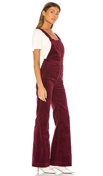 Woman wearing a burgundy corduroy jumpsuit on a white background