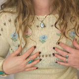 Person wearing a floral embroidered sweater with jewelry and nail polish.