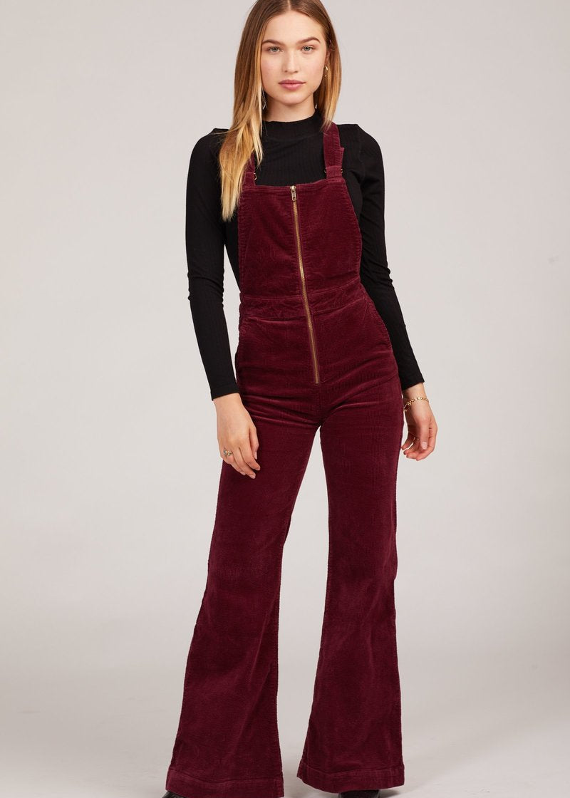 Woman wearing a burgundy velvet jumpsuit with a black top on a white background rollas overalls