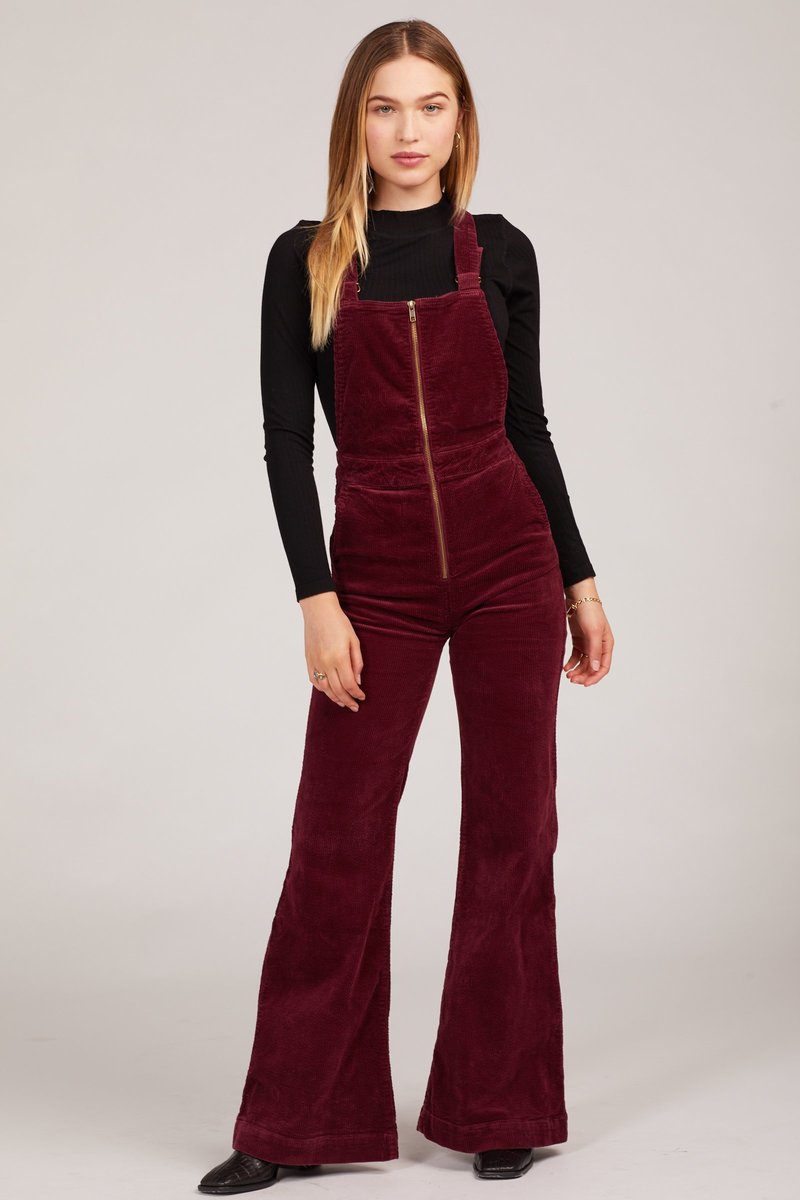 Woman wearing a burgundy velvet jumpsuit with a black top on a white background rollas overalls