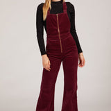 Woman wearing a burgundy velvet jumpsuit with a black top on a white background rollas overalls