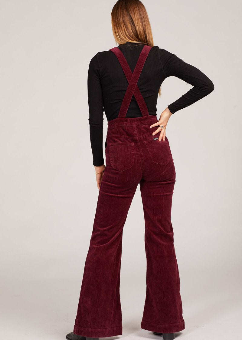 Person wearing burgundy corduroy overalls on a white background