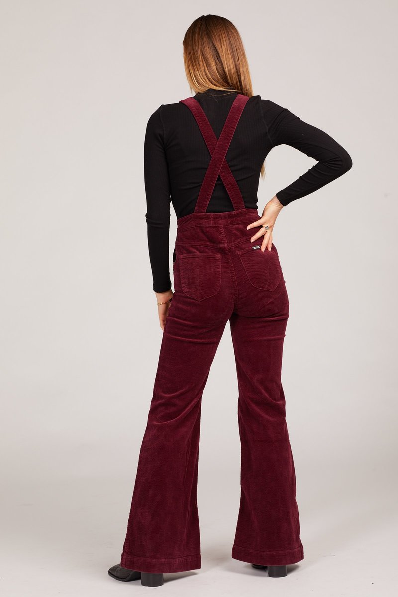 Person wearing burgundy corduroy overalls on a white background