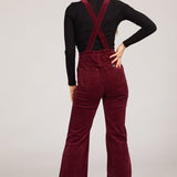 Person wearing burgundy corduroy overalls on a white background
