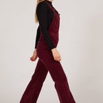 Person wearing a burgundy velvet jumpsuit with a plain background