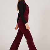 Person wearing a burgundy velvet jumpsuit with a plain background