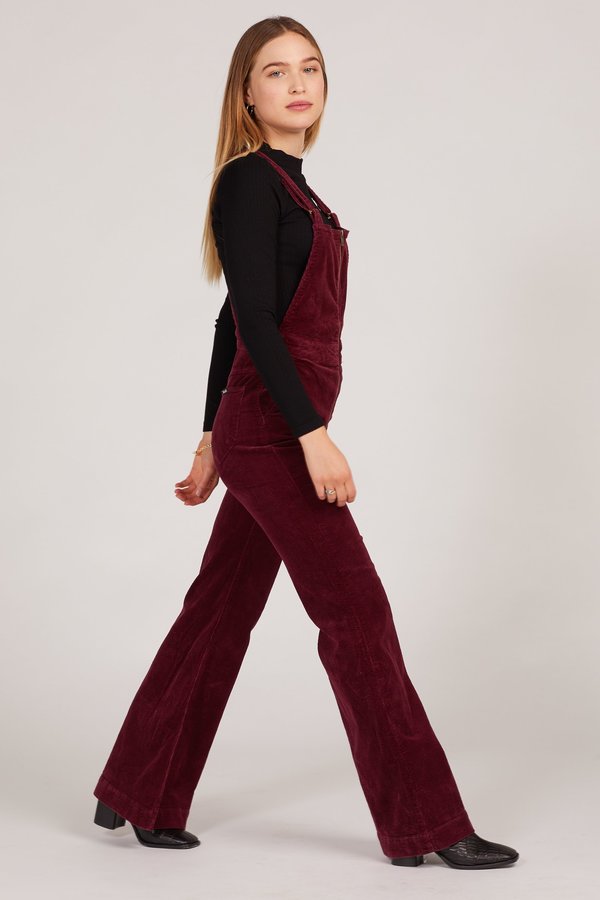 Person wearing a burgundy velvet jumpsuit with a plain background