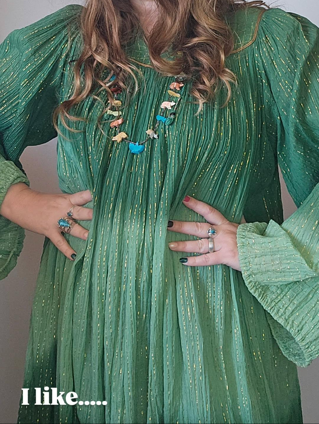 Woman wearing a green dress with puffed sleeves and a beige hat, posing with hands on hips.