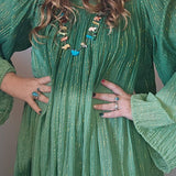 Woman wearing a green dress with puffed sleeves and a beige hat, posing with hands on hips.