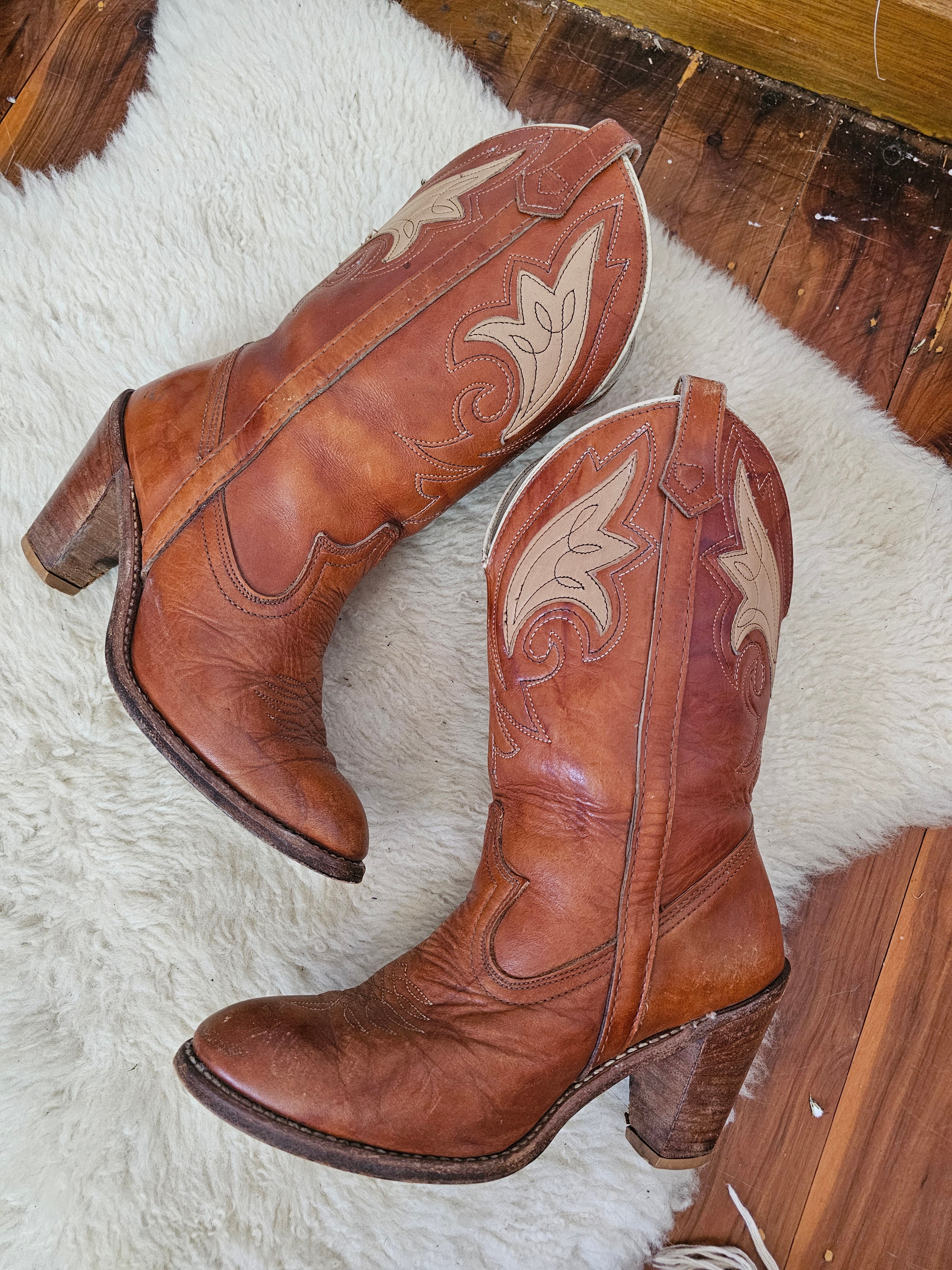 Pair of brown cowboy boots with white stitching on a white rug.