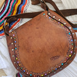 Brown leather bag with colorful studs on a striped fabric background