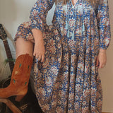 Model wearing Property of Zephyr – Sienna Long Layer Dress in blue and cream paisley print with tassel neckline and balloon sleeves, size small.