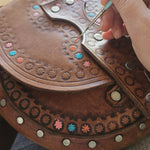 Person working on a brown leather saddle with decorative studs and patterns.