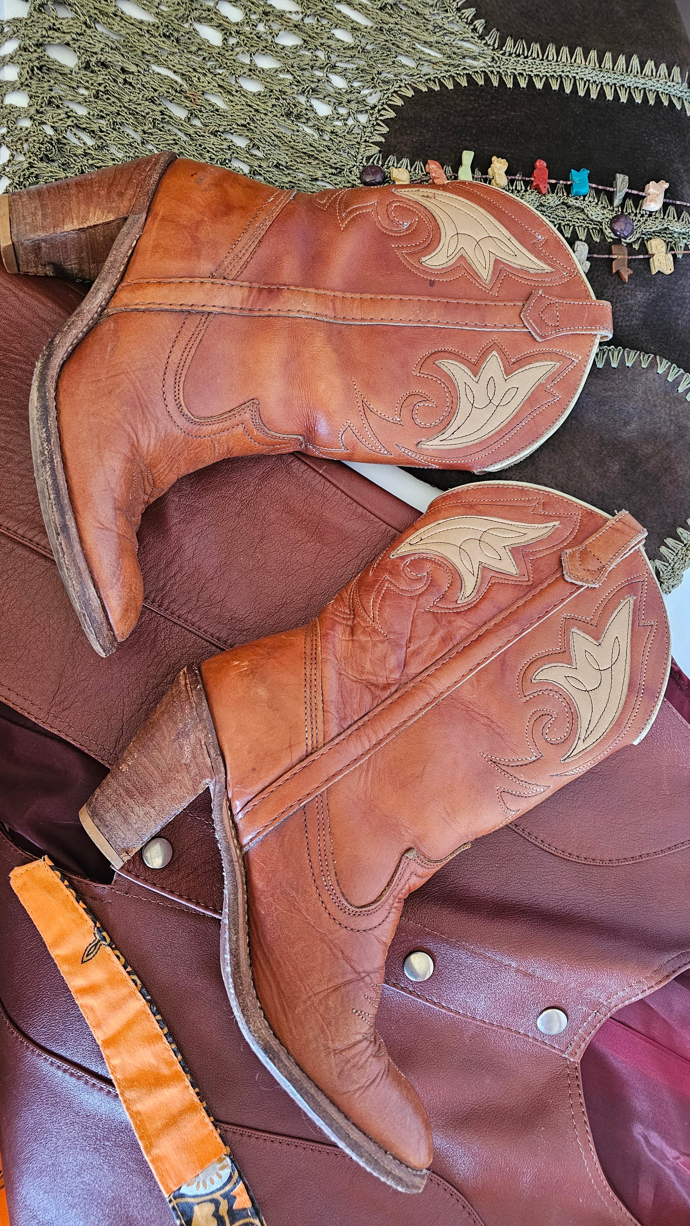 Pair of brown cowboy boots with intricate designs on a textured surface.
