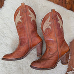 Pair of brown leather boots with decorative patterns on a white fur surface.