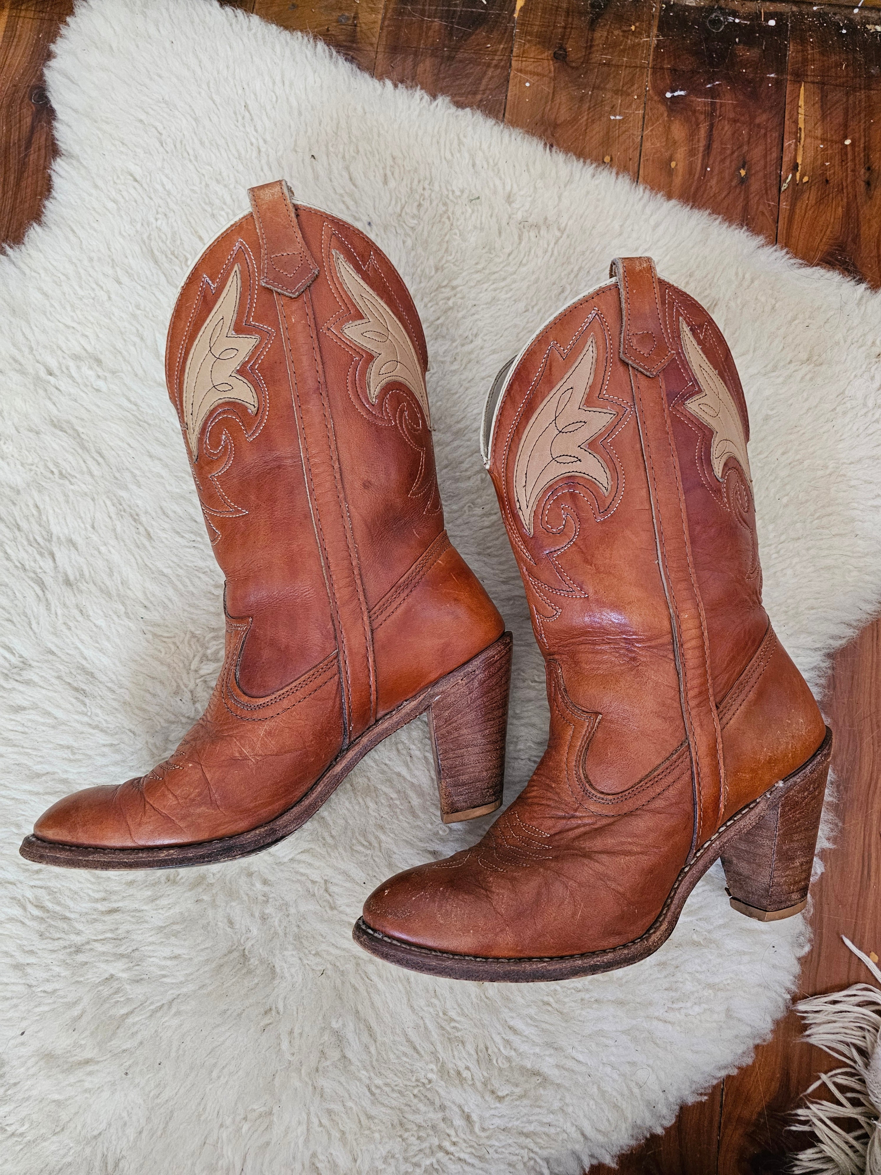 Pair of brown leather boots with decorative patterns on a white fur surface.