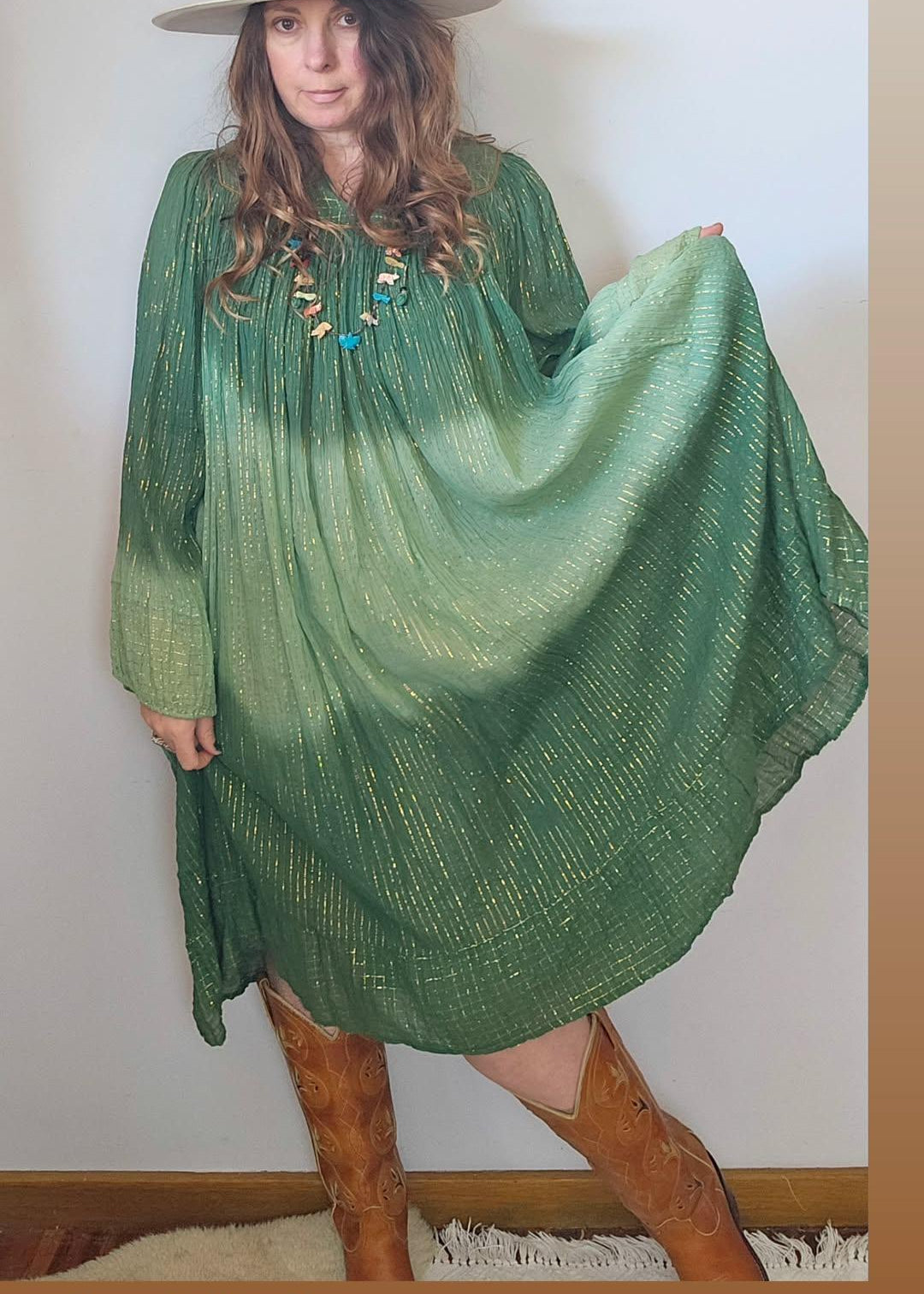 Woman wearing a green dress with gold threadwork, standing against a white wall.