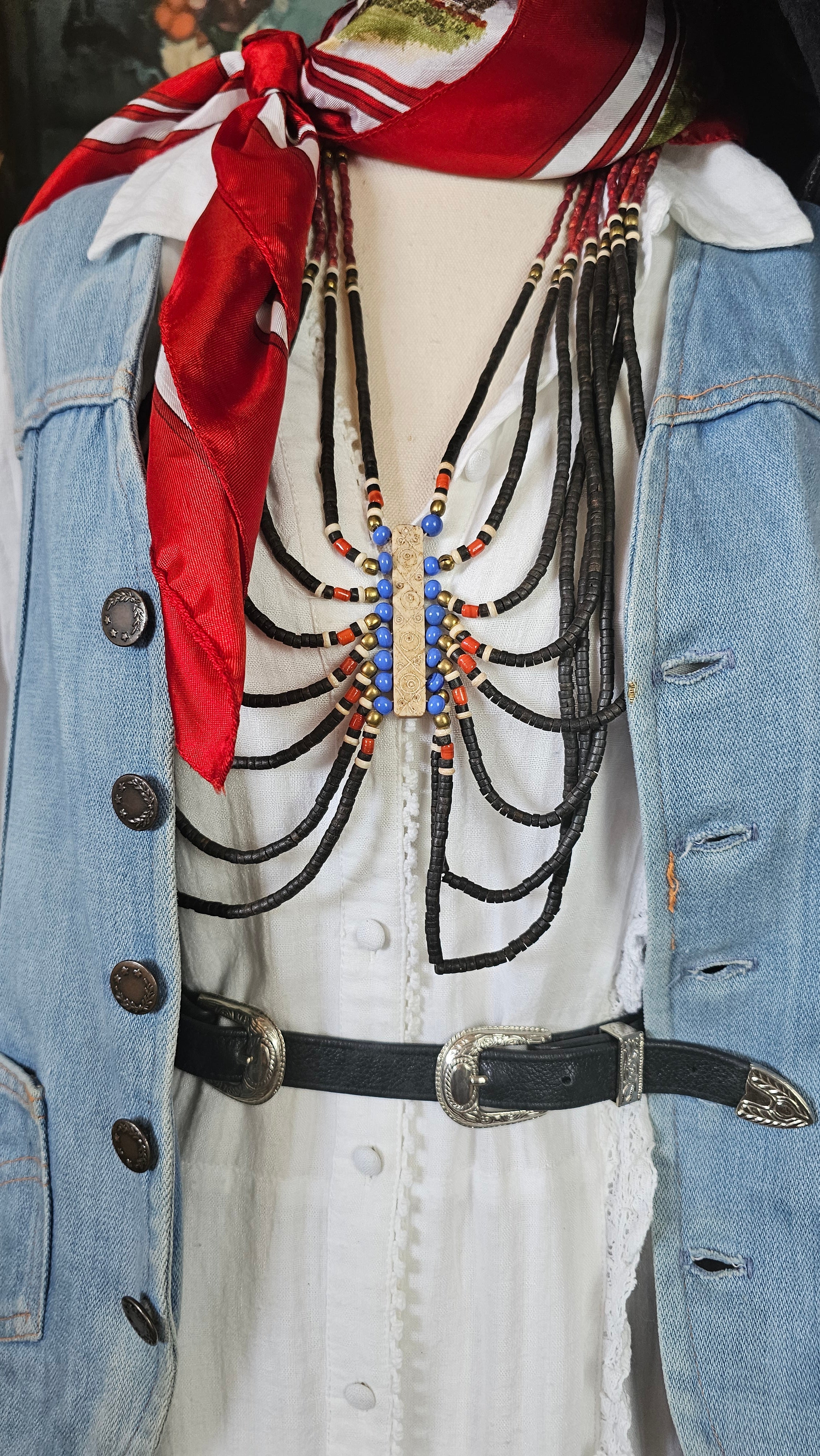 Close-up of a decorated boot with intricate patterns and a red ribbon, worn with blue jeans.