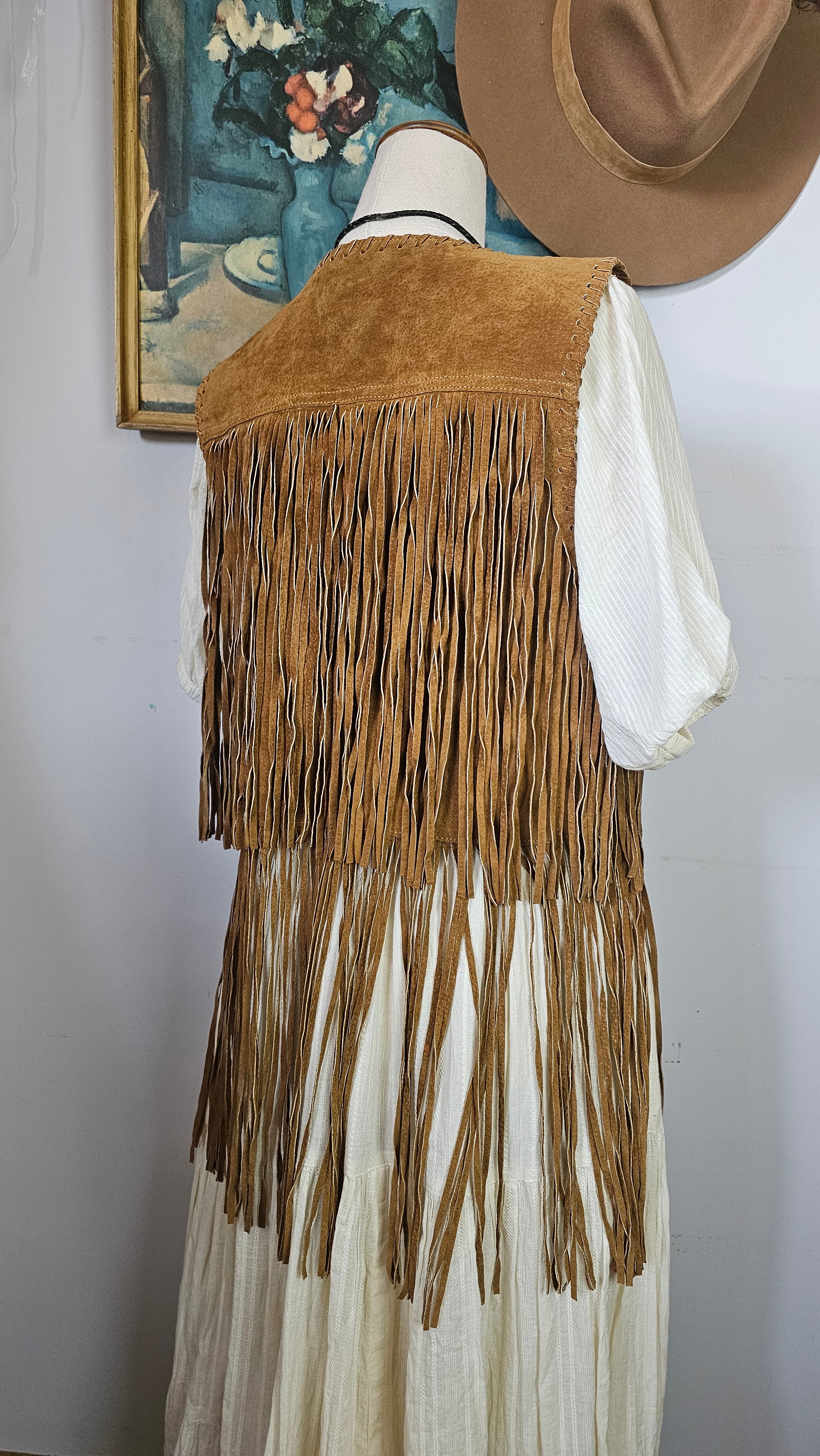 Close-up of a fringed leather bag with a hat and book in the background