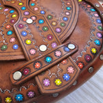 Decorative brown leather item with colorful gemstones on a textured surface