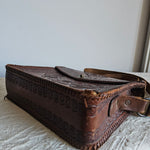 Brown leather pouch with intricate designs attached to a white surface