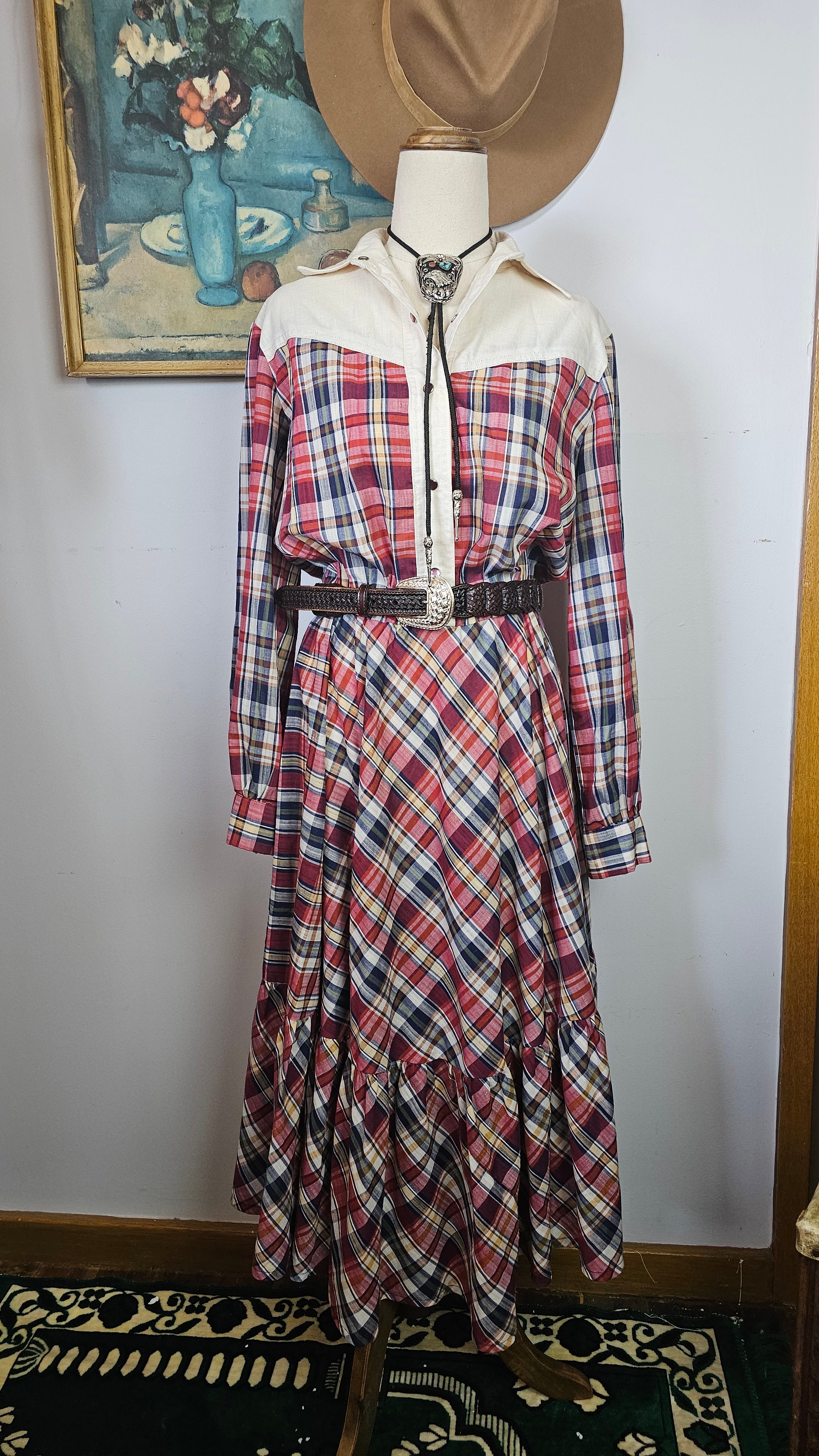Plaid dress on a mannequin with a hat, against a white wall.