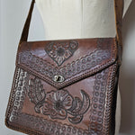 Brown leather handbag with floral embossing on a white surface