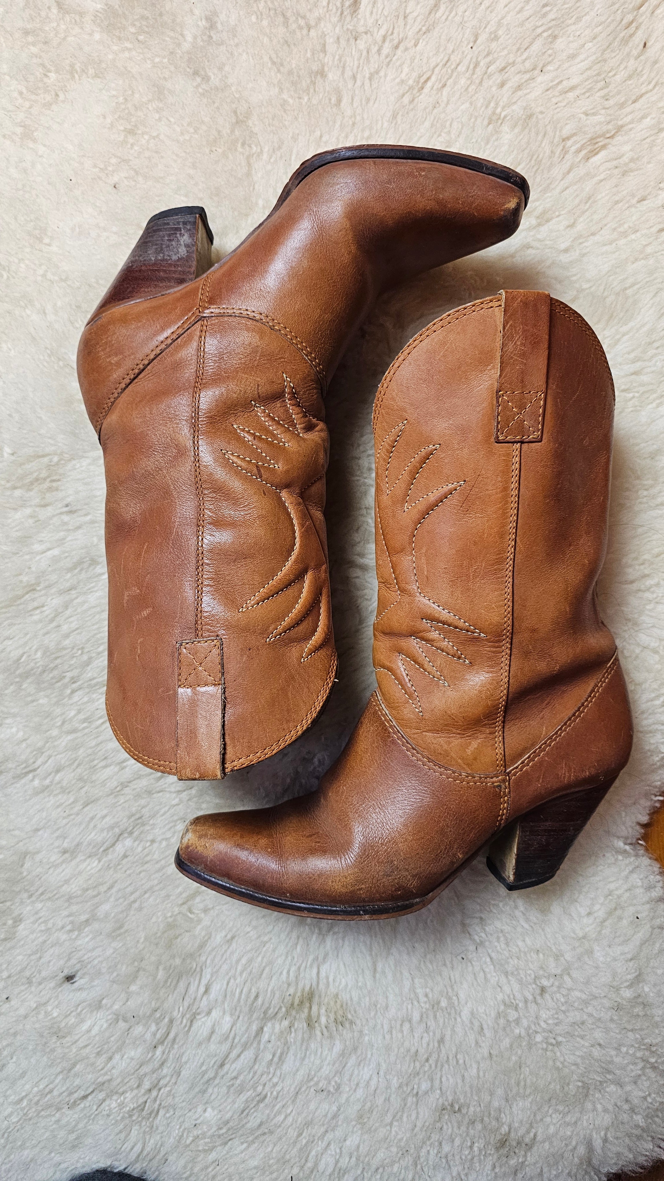 Vintage Brazilian Boots - Size 7B laid flat on a sheepskin rug, showcasing the curved heels and detailed stitching of these 70s leather boots.
