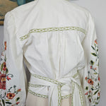 White embroidered dress on a mannequin with a brown hat and floral fabric in the background