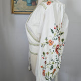 White embroidered blouse with floral patterns on a plain background