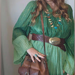 Woman in a green dress with a brown belt and a brown leather bag, wearing a beige hat.