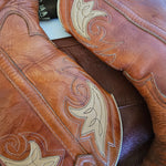Close-up of a brown leather saddle with intricate white stitching on a wooden surface.