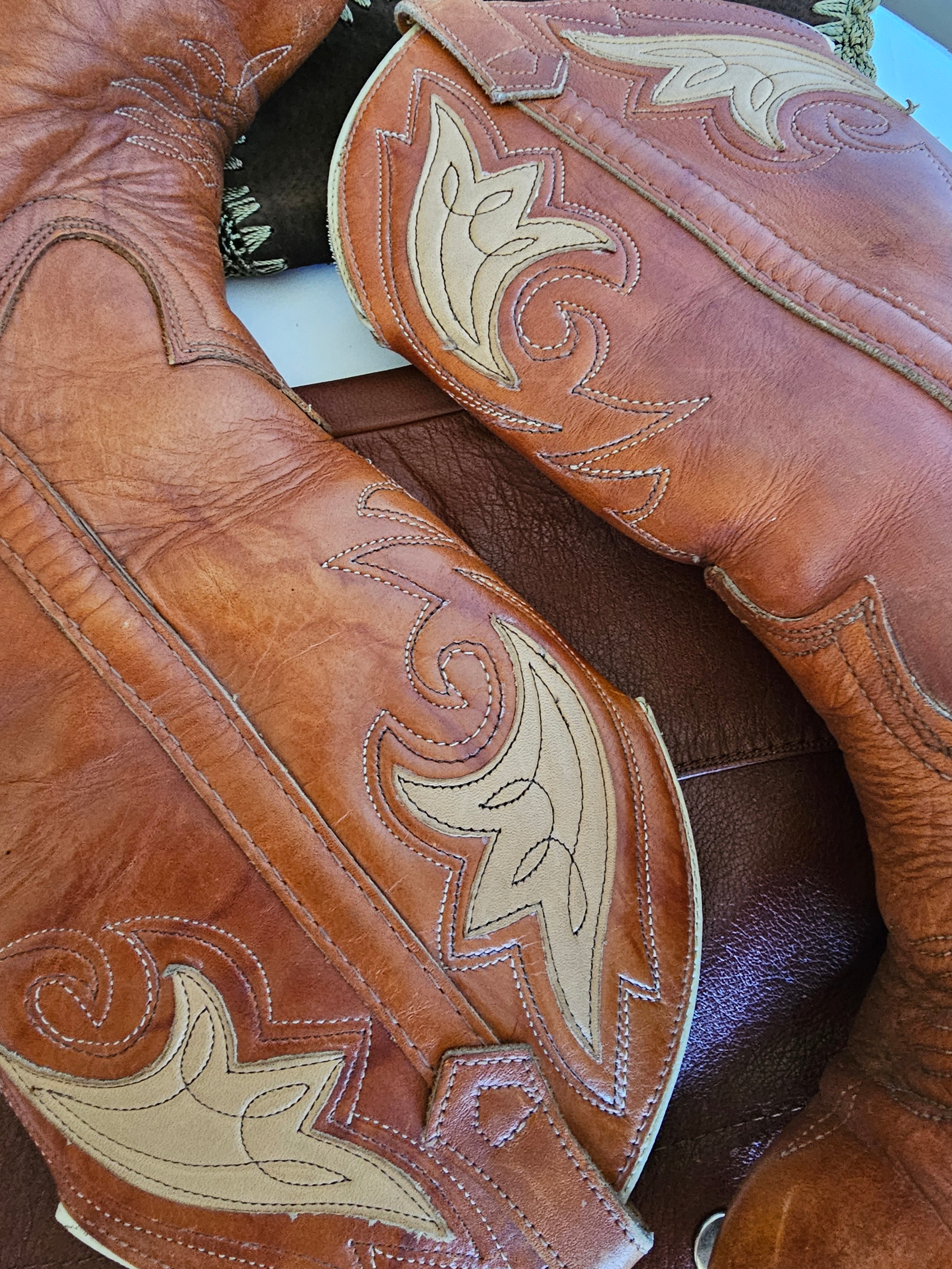 Close-up of a brown leather saddle with intricate white stitching on a wooden surface.