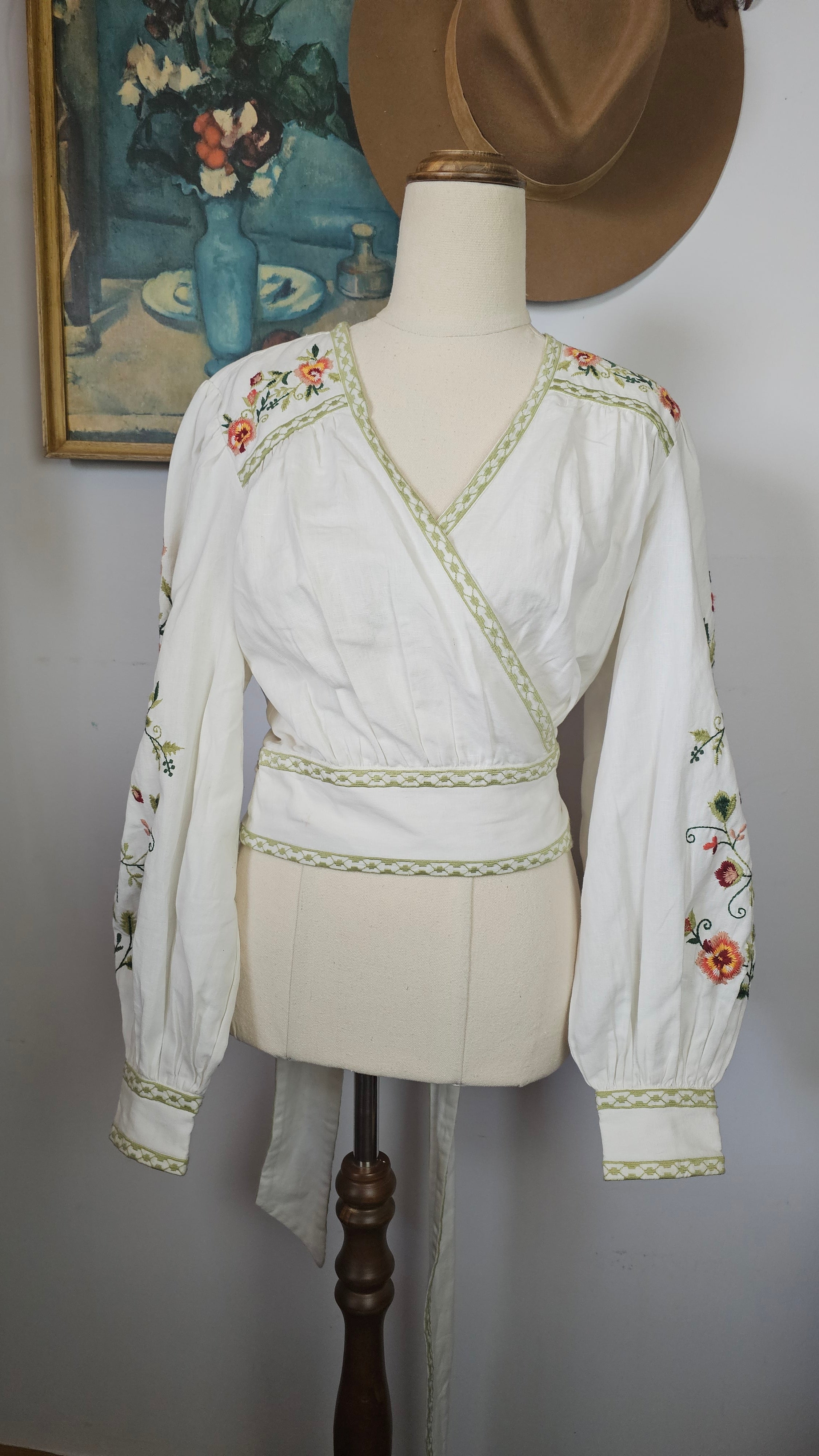 Traditional embroidered garment on a mannequin with a hat and fabric in the background