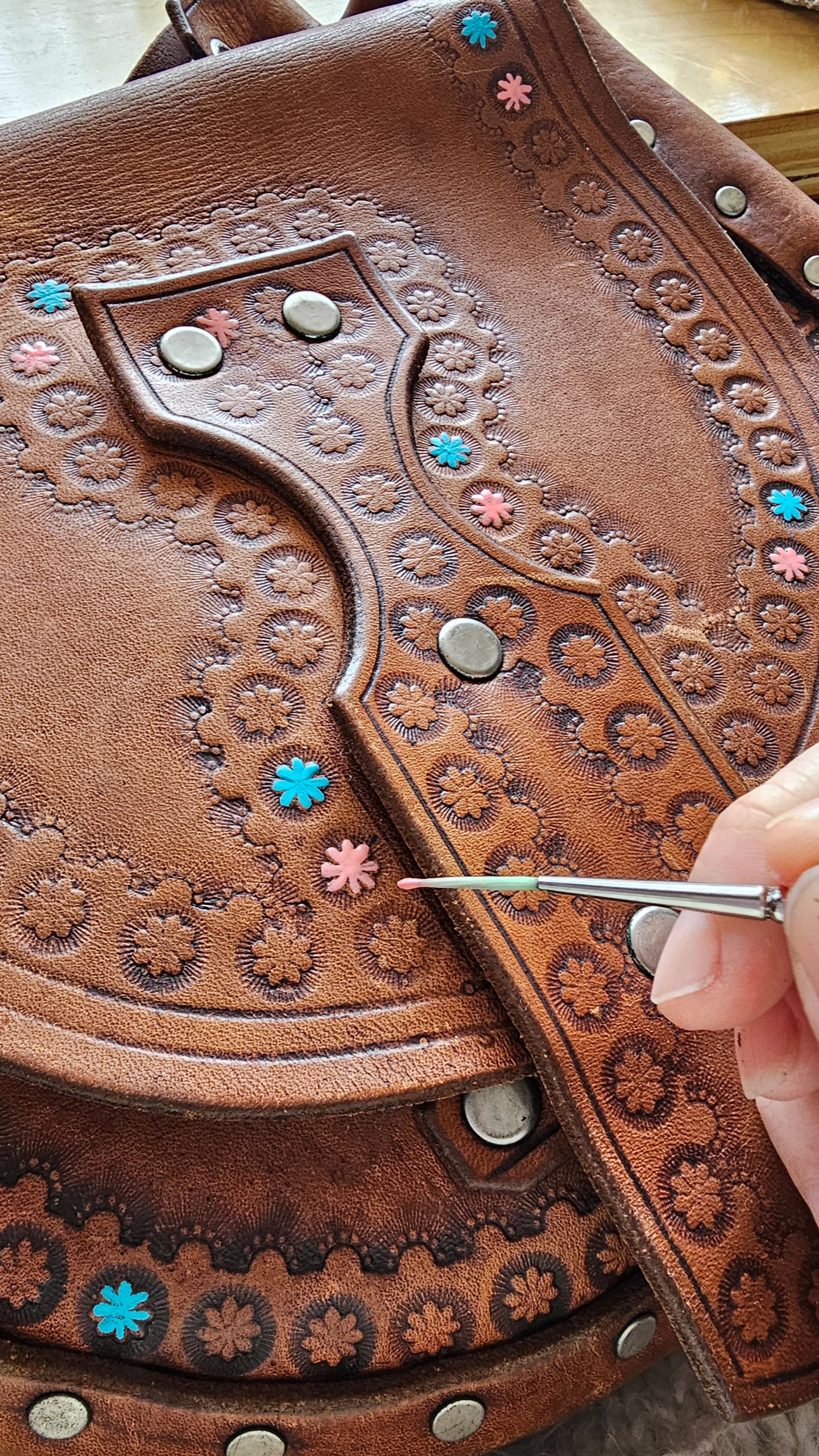 Close-up of a hand stitching intricate patterns on a brown leather bag.