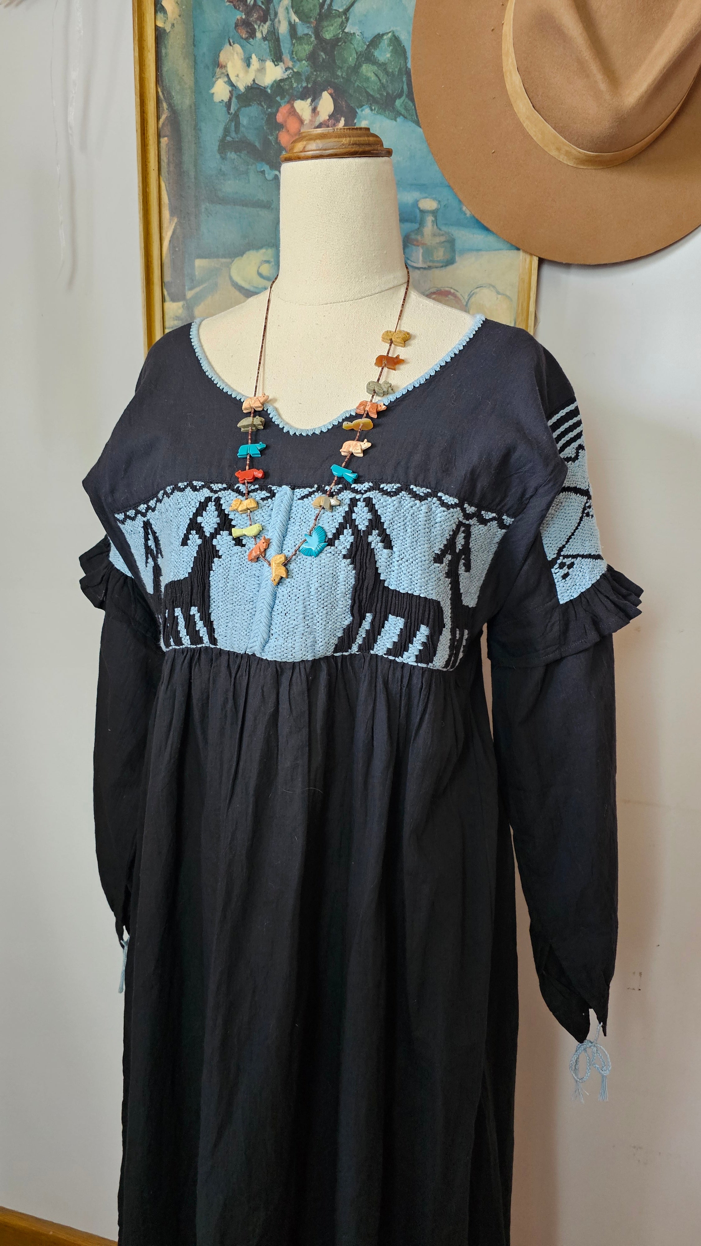 Black dress with colorful embroidery on a mannequin against a neutral background