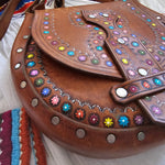 Brown leather bag with colorful gemstones and decorative studs on a white background