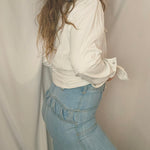 Person wearing a white shirt, blue jeans, and a brown hat lying on a beige surface.