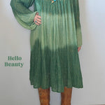 Woman wearing a green dress with a gradient effect, standing against a plain wall.