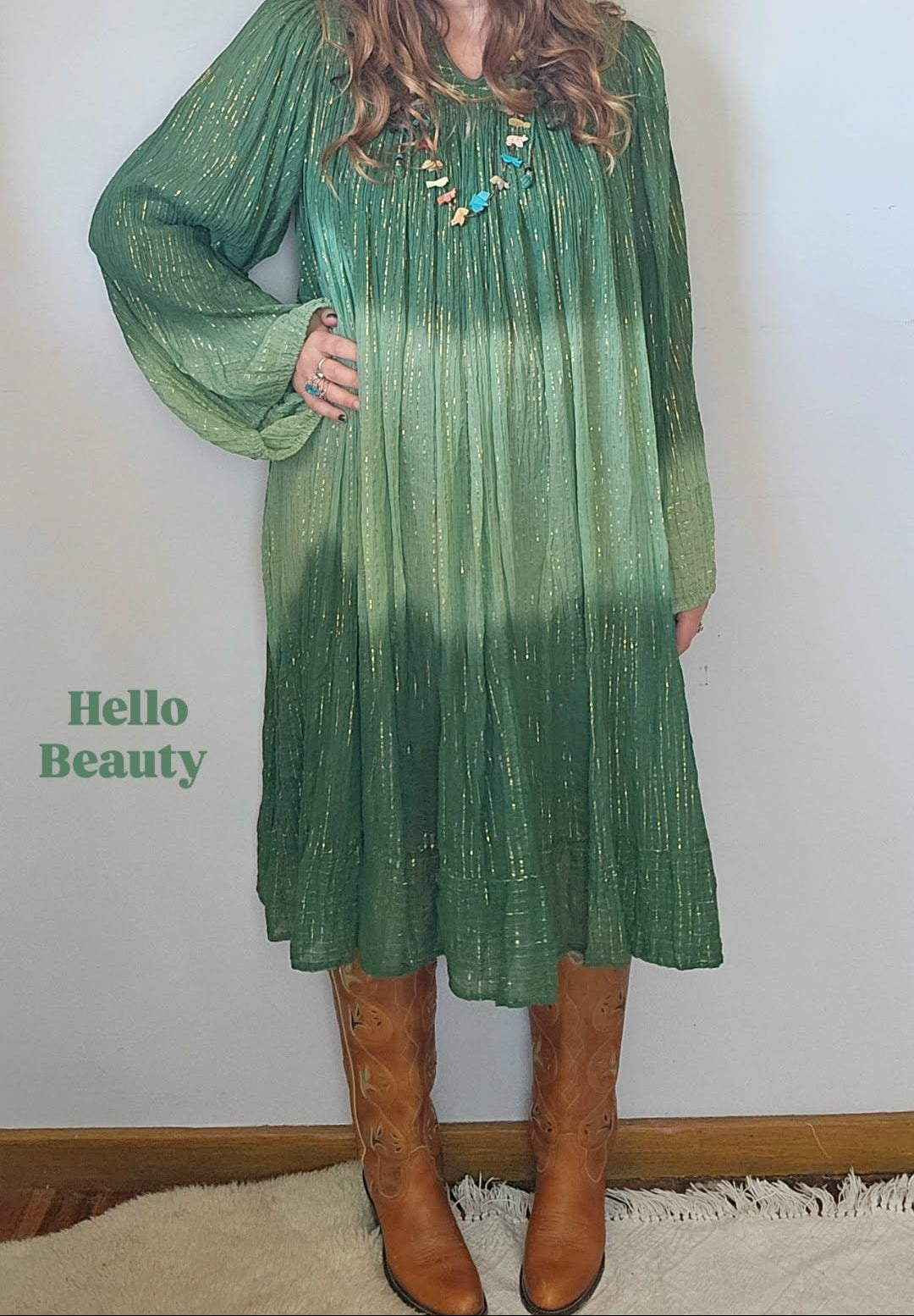 Woman wearing a green dress with a gradient effect, standing against a plain wall.