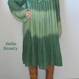 Woman wearing a green dress with a gradient effect, standing against a plain wall.