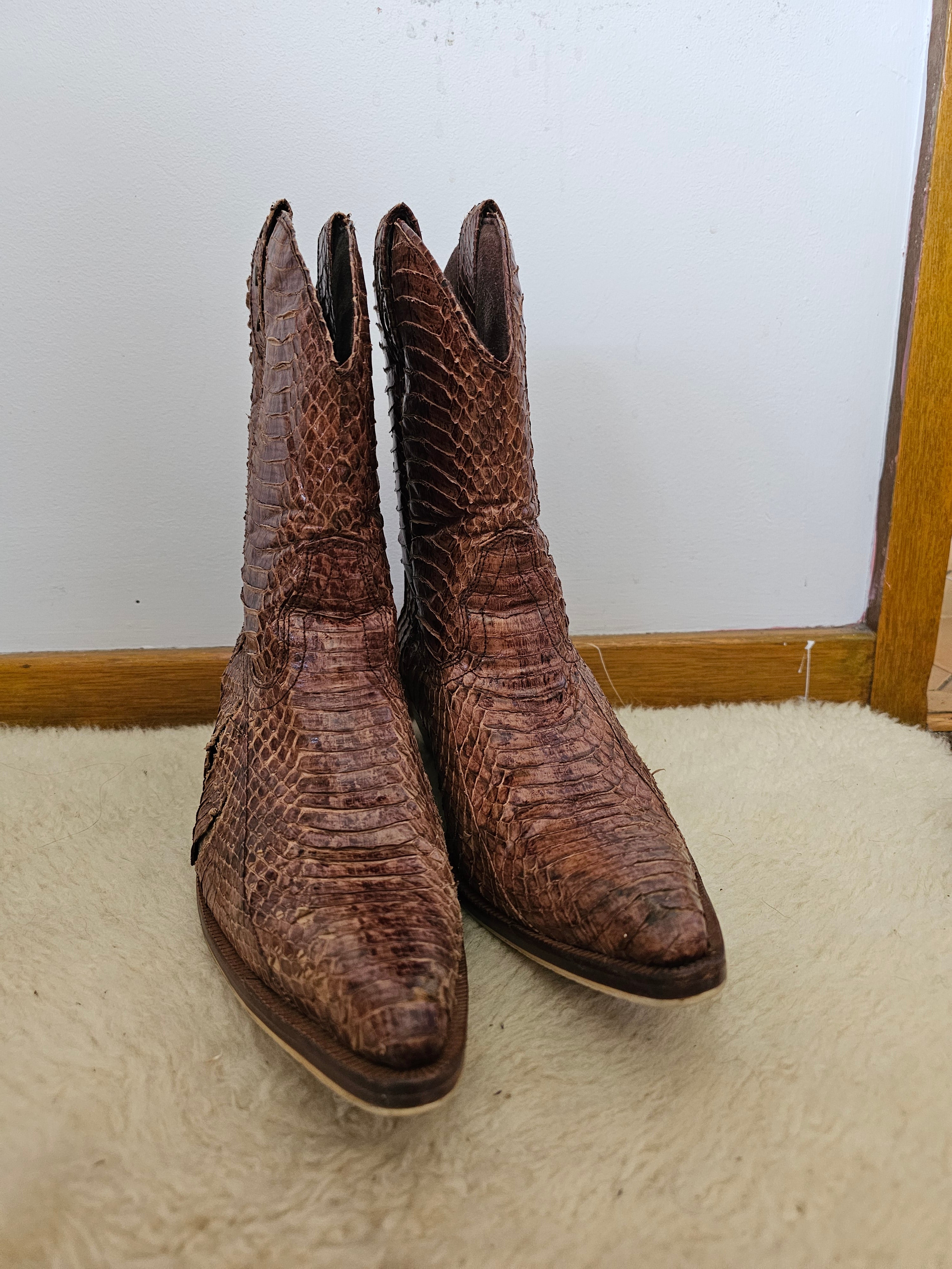 Pair of brown cowboy boots on a white surface with a wooden frame.