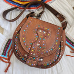 Brown leather bag with colorful gemstones on a textured surface