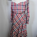 Plaid dress on a mannequin against a white wall with a framed picture and hat in the background.
