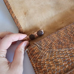 Close-up of a hand holding a brown leather product with stitching details