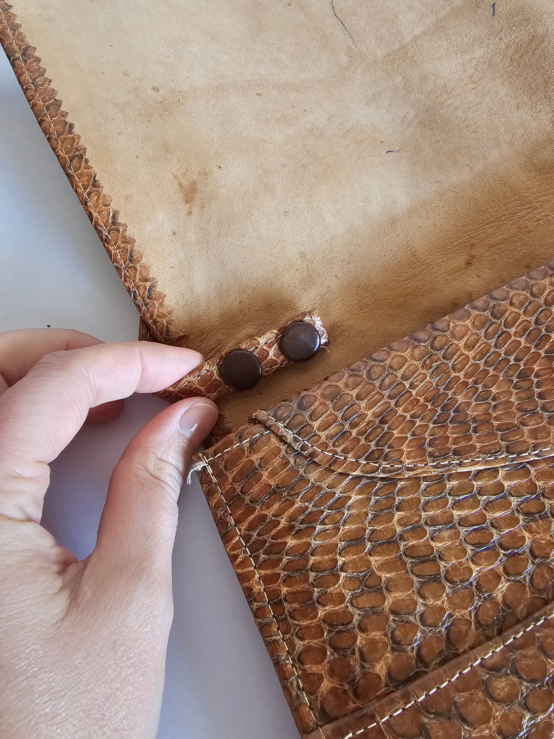 Close-up of a hand holding a brown leather product with stitching details