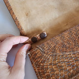 Close-up of a hand holding a brown leather product with stitching details