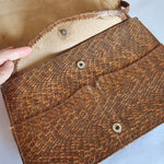 Brown leather clutch with snake skin pattern on a light blue background