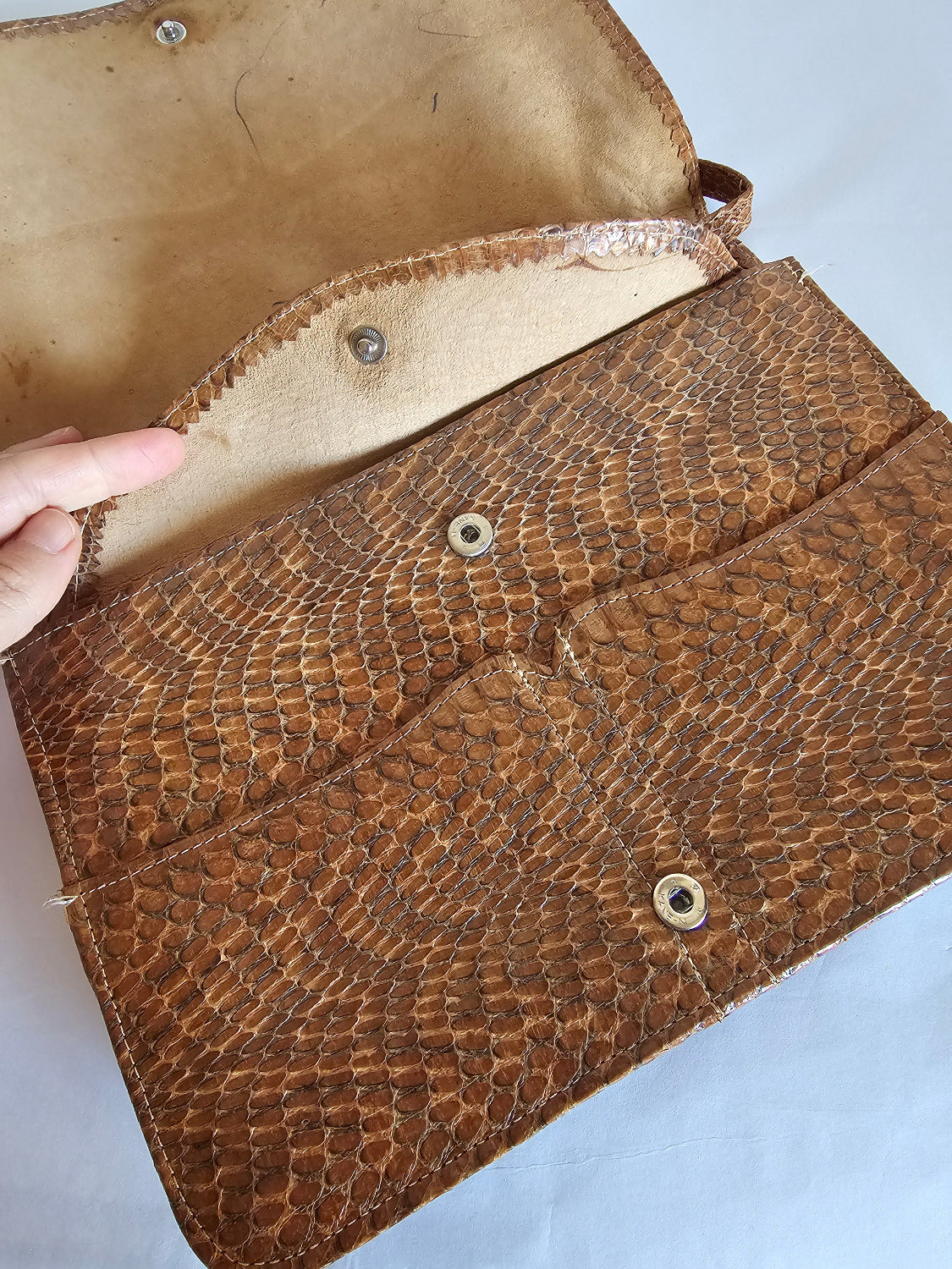 Brown leather clutch with snake skin pattern on a light blue background
